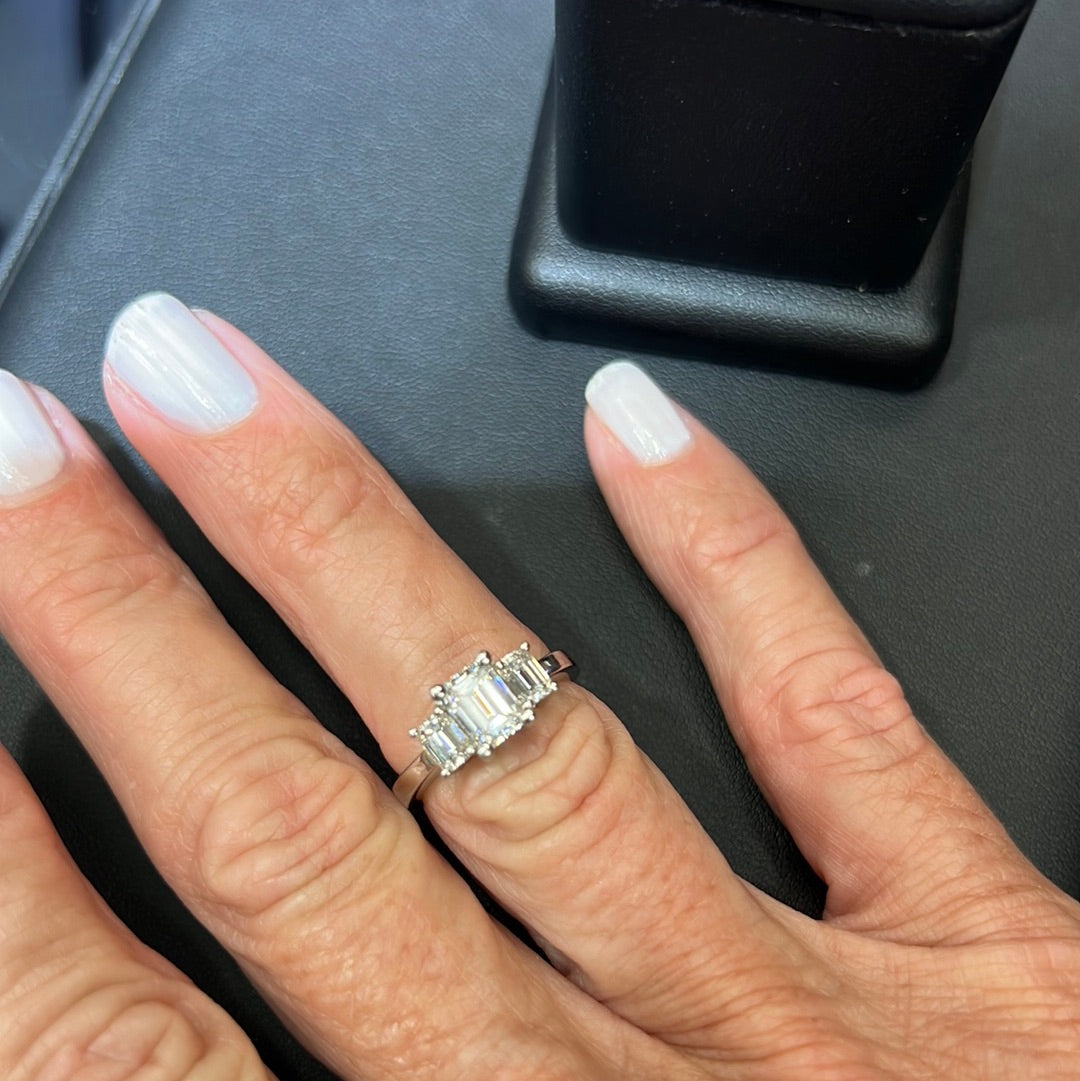 1.75 ct Center Stone Emerald Cut Diamond H VS2 Set in Platinum with 2 side diamonds on a hand with grey blue painted fingernails