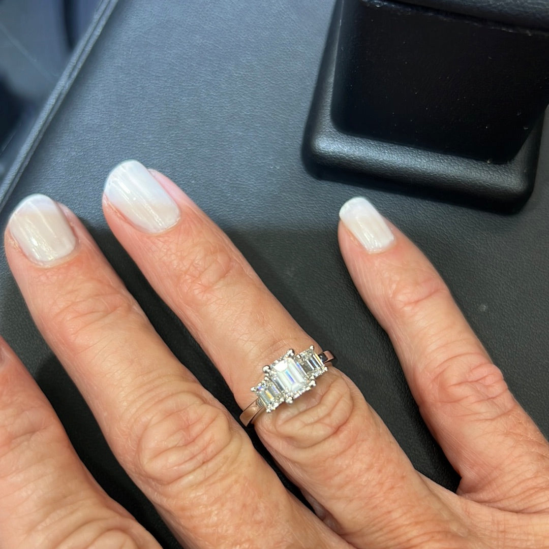 1.75 ct Center Stone Emerald Cut Diamond H VS2 Set in Platinum with 2 side diamonds on a hand with grey blue painted fingernails