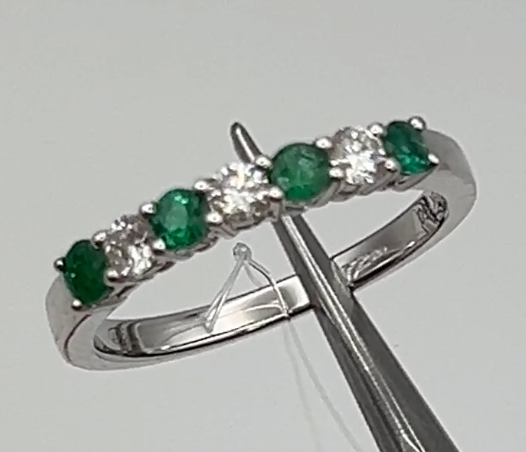 a close up of a ring with small emerald green round stones with white diamonds